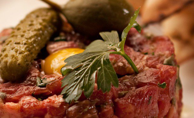steak tartar with a green pickle and a green olive on top. Serviced with toasted pita bread