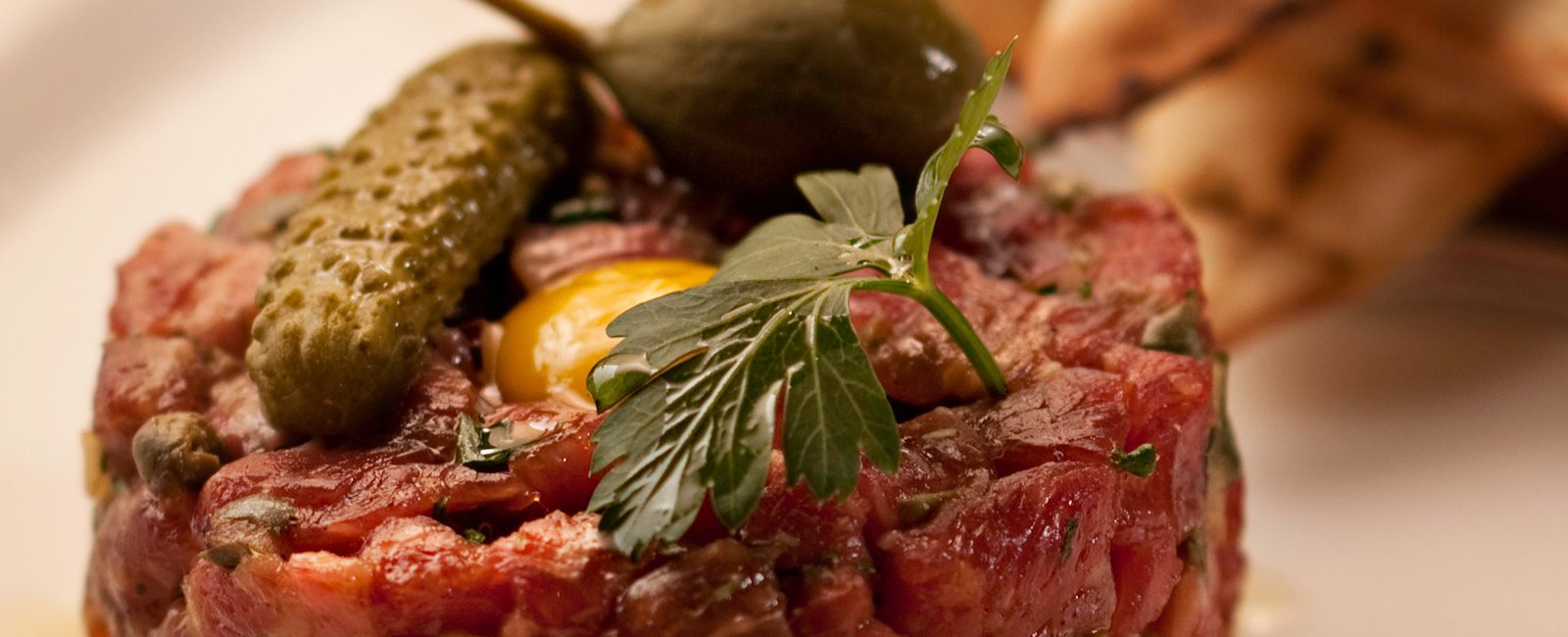 steak tartar with a green pickle and a green olive on top. Serviced with toasted pita bread