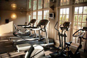 Sun-filled fitness center with a treadmill, ellipticle, and a spin bike.